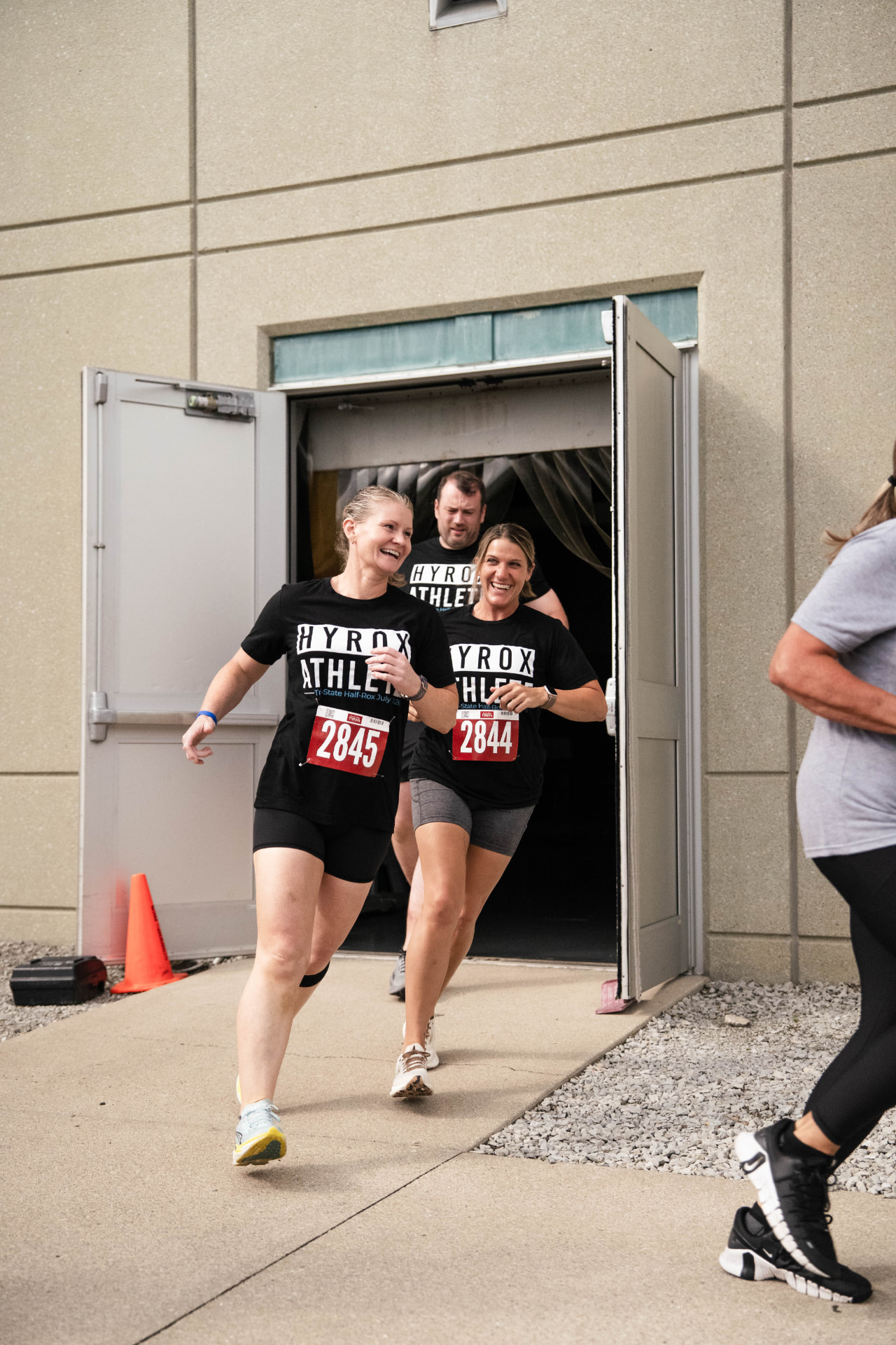 Athletes in Hyrox race bibs running out of the gym doors